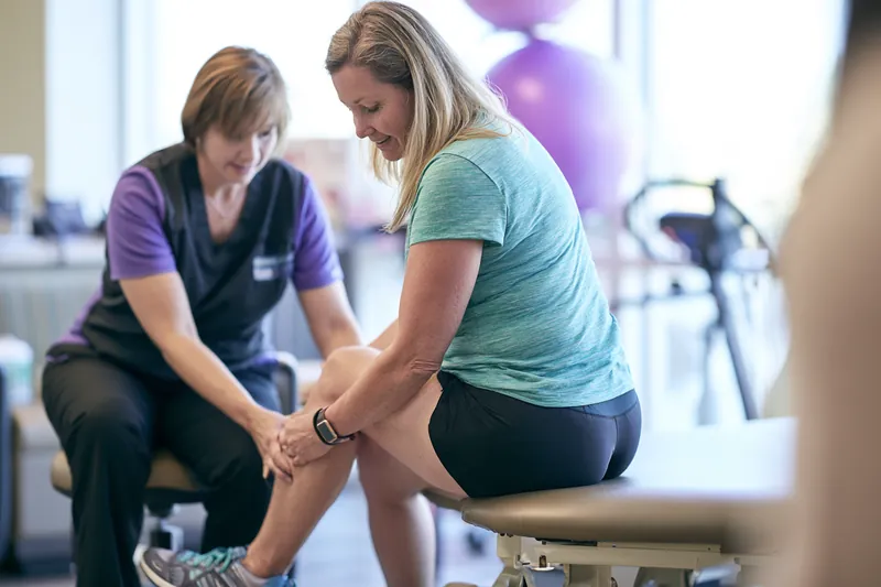 Over-the-shoulder view of a physical therapist guiding a woman in her 40s through a knee exercise, a treatment some patients fund with a medical loan