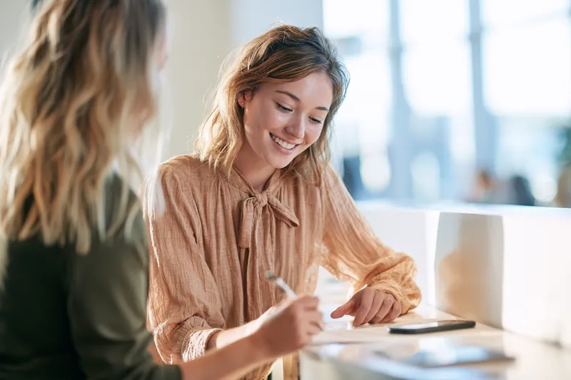 Woman in her 20s signing an apartment lease with a leasing agent at a bright, modern front counter